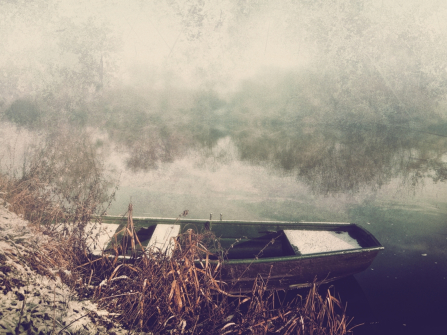Ein kleines Boot am schneebedeckten Ufer eines kleinen Flusses, das mit analogen und künstlerischen Effekten bearbeitet wurde.